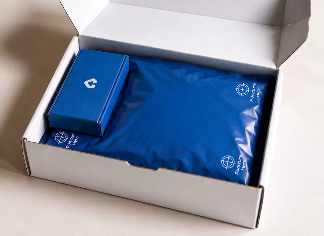 An open white corrugated shipping box holding a small blue CentiPack carton beside a blue gel pack marked "Puncture here".