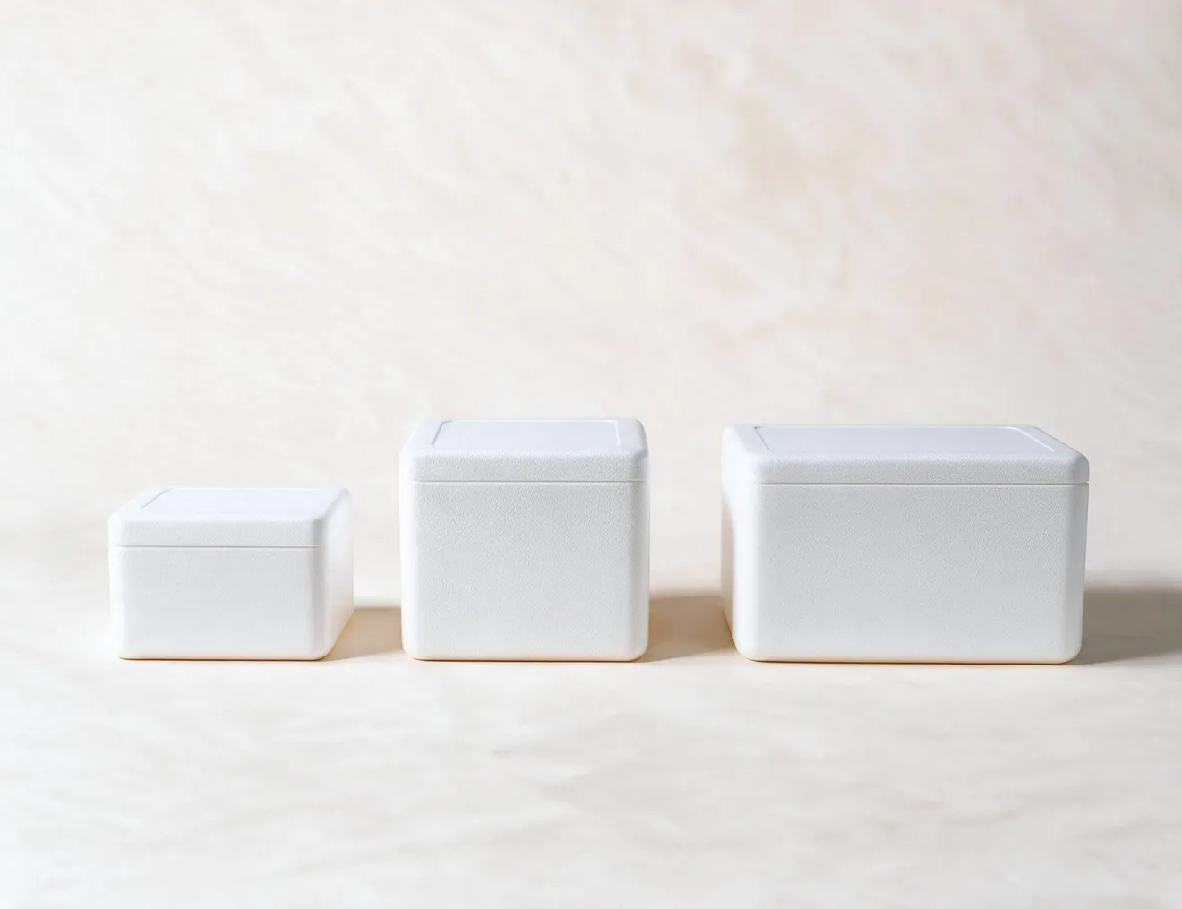 Three white EPS foam coolers closed and side by side on a cream ground, shown in ascending size.