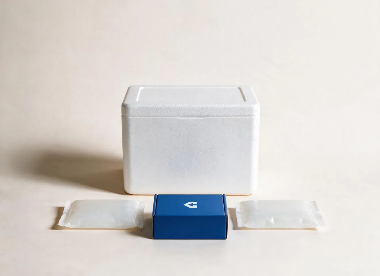 A closed white EPS foam cooler with its pack-out laid out in front of it — two gel packs flanking a small navy CentiPack carton.