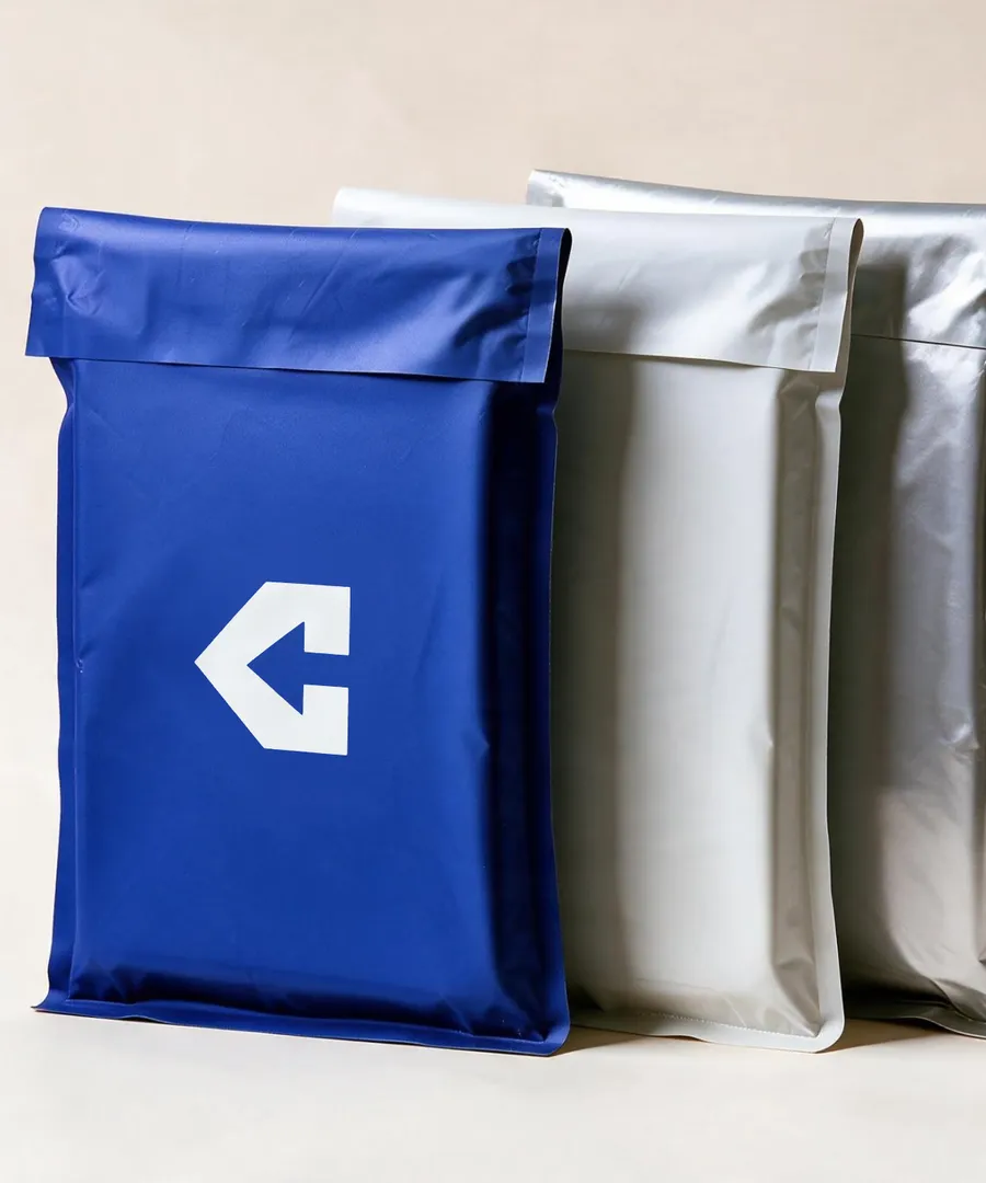 Three insulated mailers standing one behind the other on a cream ground — navy in front printed with the CentiPack arrow, then white and silver.