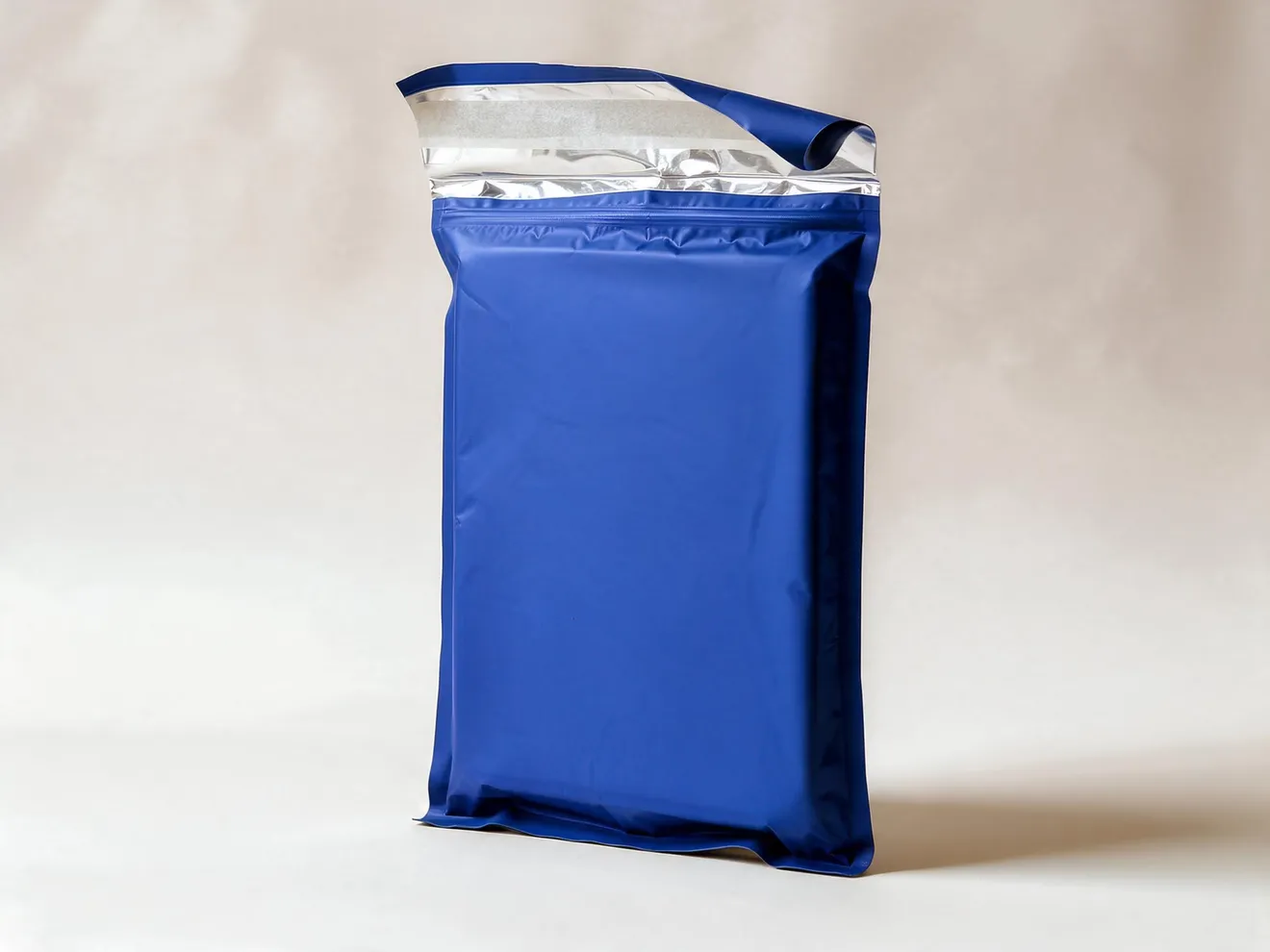 An expanded navy insulated mailer standing upright, its top flap peeled back to show the silver inner lining and the adhesive strip beneath the release liner.
