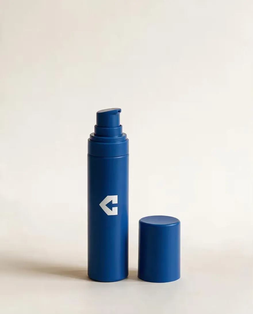 A navy airless pump bottle with its cap alongside.